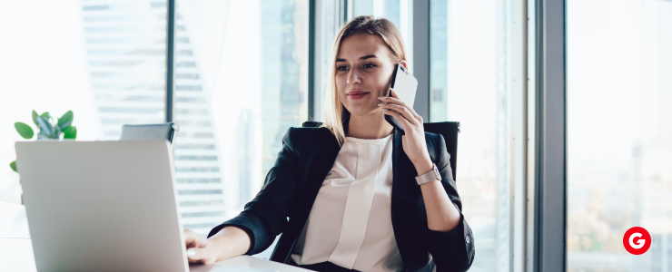 A woman in a business suit sits at a desk, working on a laptop in a professional office setting.